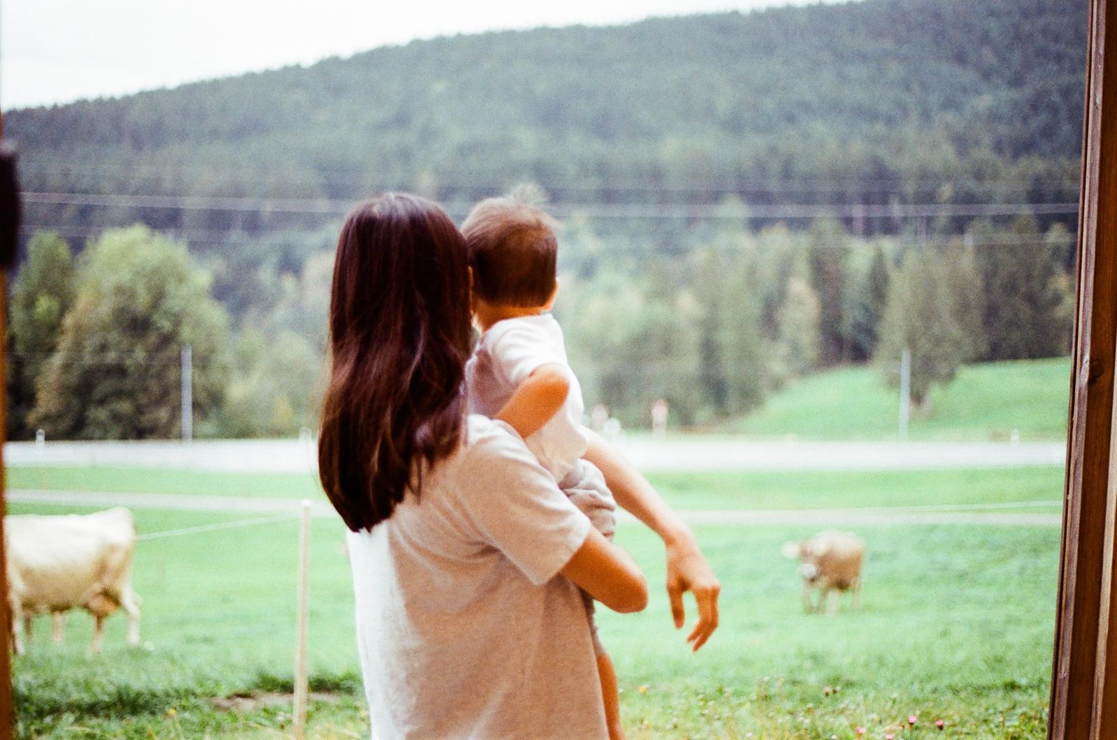 Madre sosteniendo a su hija frente a un paisaje verde